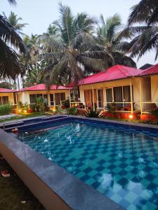 a swimming pool in front of a house with palm trees at The Sunbliss Cottages in Morjim