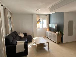 ein Wohnzimmer mit einem schwarzen Sofa und einem TV in der Unterkunft Rez-de-chaussée bord de piscine in Los Tomases