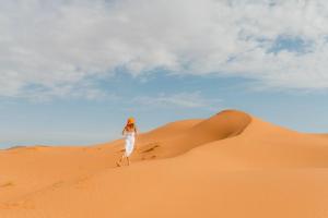 a woman standing on a sand dune in the desert at Sahara Berber Camp - Mhamid Discovery Camp in Mhamid el Rhozlane
