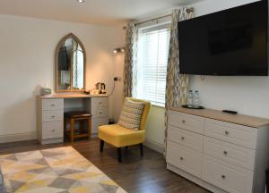 a bedroom with a dresser with a tv and a yellow chair at Tudor Lodge Bed & Breakfast in Manorbier +64 photos