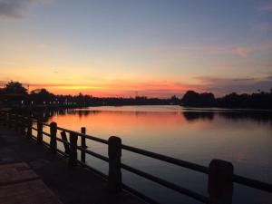 a sunset over a body of water with a fence at Baan Songsri in Amphawa