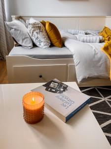 a candle and a book on a table next to a bed at Apartament White in Giżycko