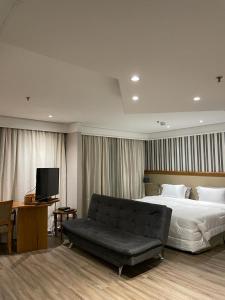 a bedroom with a bed and a couch and a television at Suite Radisson Vila Olimpia in Sao Paulo
