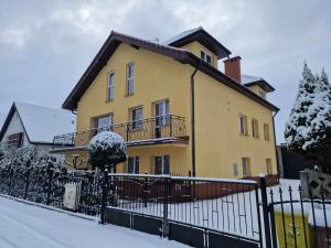 una casa amarilla con una cerca en la nieve en AGNES, en Grzybowo