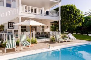 a house with a pool and chairs and an umbrella at Southern Cross Beach House in Plettenberg Bay