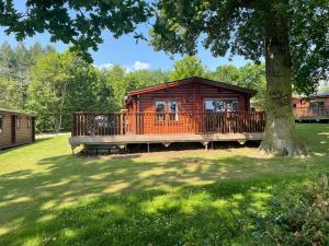 a log cabin with a large deck next to a tree at The Fairways, Kenwick Retreats in Louth