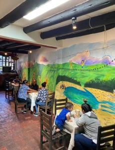 grupa ludzi siedzących przy stolikach przed muralem w obiekcie Beija Flor Hostel w mieście Villa de Leyva