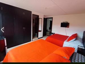a bedroom with two beds with orange sheets and a television at Casa de Huéspedes Santa María Hotel in Bogotá