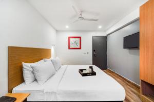 a bedroom with a white bed with a tv on the wall at Townhouse De Alphabet Tirupati in Tirupati