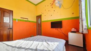 a bedroom with an orange wall with a bed and a tv at Sea Front Homestay in Magong