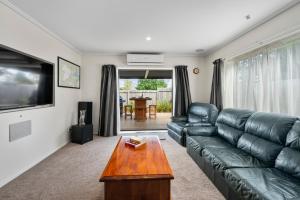 a living room with a black leather couch and a table at The Tin Hut - Kinloch in Kinloch