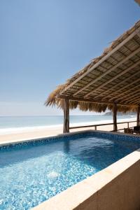 a swimming pool with a straw umbrella and the beach at Hotel Sanmara in La Sabrosa