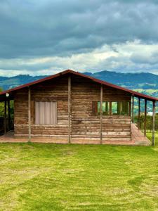 une cabane en rondins avec un toit rouge sur un champ vert dans l'établissement Refugio Aventura, hermosa cabaña y acogedores glampings en Tabio, cerca a Bogotá, à Tabio