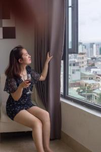 una mujer sentada en una silla mirando por una ventana en Lis Hotel en Da Nang