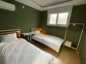 濟州的住宿－hola! Hostel，绿色客房的两张床,设有窗户