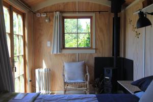 a bedroom with a bed and a chair and a window at The Bird Hide - rustic luxury by the water in Dunedin