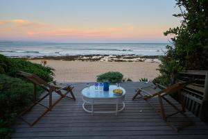 una mesa y sillas en una terraza de madera con la playa en Soul Searchers en Jeffreys Bay