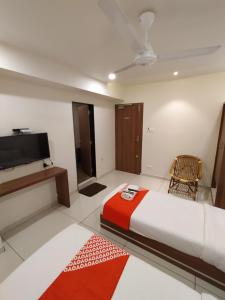 um quarto com uma cama, uma televisão e uma cadeira em Surbhi Hotel And Restaurant em Rajkot