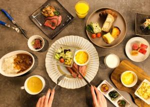 a table with plates of food and people holding utensils at LUXCARE HOTEL in Osaka