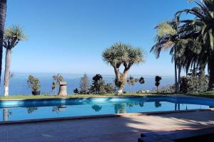 a swimming pool with palm trees and the ocean in the background at Espectacular Villa con piscina y vistas al valle in Cruz Santa