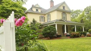 a yellow house with a white fence and pink flowers at The Dailey Renewal Retreat B & B in Greensboro