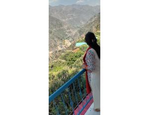 a woman standing on a balcony looking out at the mountains at Ashgrove village resort, Kempty fall in Lakhwār