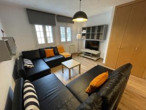 salon z czarną skórzaną kanapą i pomarańczowymi poduszkami w obiekcie Loft con WiFi y Parking en el corazón de Sierranevada w mieście Sierra Nevada