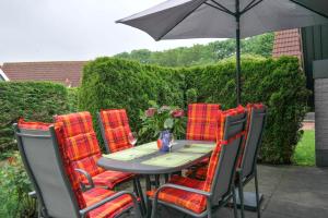 a table with red cushioned chairs and an umbrella at am Deich 6 pers House with a private terrace behind a dike by the Lauwersmeer in Anjum