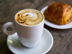 a cup of coffee sitting on a table with a pastry at Hotel Sofitel Los Angeles at Beverly Hills in Los Angeles