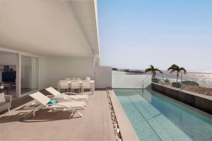 a house with a swimming pool with chairs and the ocean at Royal Hideaway Corales Suites in Adeje