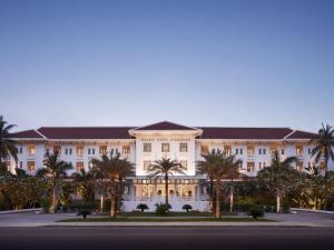 een groot gebouw met palmbomen ervoor bij Raffles Grand Hotel d'Angkor in Siem Reap