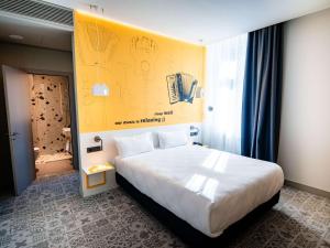 ein Schlafzimmer mit einem großen Bett mit gelber Wand in der Unterkunft Ibis Styles Sibiu Arsenal in Sibiu