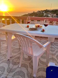 een witte tafel en stoelen met wijnglazen en de zonsondergang bij Blue Paradise Apartment in Ribeira Brava