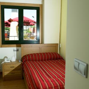 a bed in a room with a window and a red blanket at Pensión Pousada Chiquitin in Melide