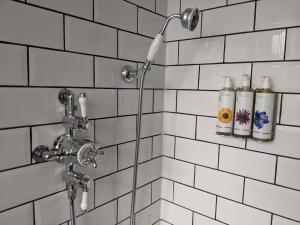 a shower with four bottles on a white tiled wall at Luxury Cottage with Swimming Pool in Bredon +34 photos
