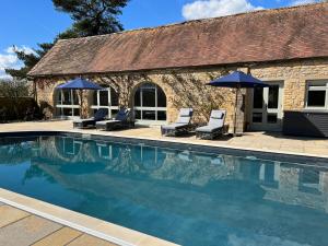 a swimming pool with two chairs and umbrellas next to a building at Two Luxury Cosy Cottages in Tewkesbury