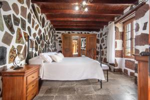um quarto com uma cama branca e uma parede de pedra em El patio canario em Firgas