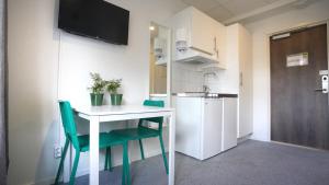 una pequeña cocina con una mesa blanca y sillas verdes en Forenom Hostel Gothenburg Säve en Gotemburgo