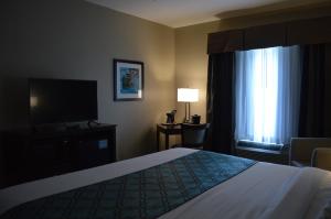Heritage Place Hotel and Suites في DeQuincy: غرفة فندقية بسرير وتلفزيون بشاشة مسطحة
