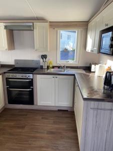 a kitchen with white cabinets and a stove and a sink at Ger-Y-Bwlch - Spacious static on 5star site with Swimming Pool in Benllech