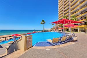 a swimming pool next to the beach with chairs and umbrellas at Sonoran SKY #910 in Puerto Peñasco