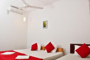 2 Betten in einem weißen Zimmer mit roten Kissen in der Unterkunft Sea Way Hotel in Nilaveli
