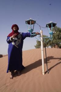 Una mujer parada junto a una luz en el desierto en Green Camp Sahara, en Mhamid