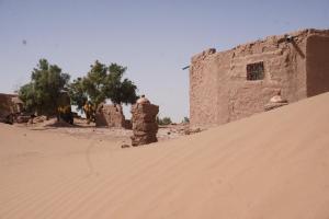 un hombre parado frente a un edificio en un desierto en Green Camp Sahara, en Mhamid