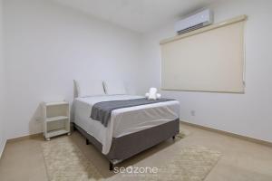 a white bedroom with a bed and a large screen at Aconchegante apartamento bem mobiliado PDM005 in Porto Seguro