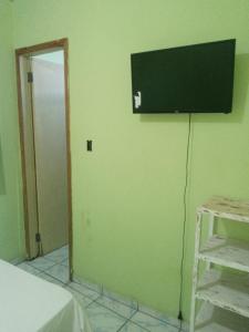 Habitación con TV en una pared verde en Egbirin Pousada en Ilhéus