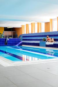 a woman sitting on a couch next to a swimming pool at ibis Styles Relax Roznov pod Radhostem in Rožnov pod Radhoštěm