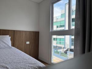 1 dormitorio con cama y ventana grande en B235 - Apartamento com 02 suítes novo em Bombinhas en Bombinhas