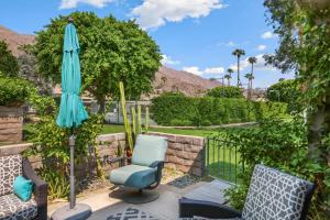 a patio with a blue umbrella and chairs and a fence at Eclectic & Comfortable Canyon Corridor - A Ryson Property in Palm Springs