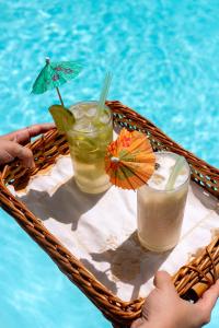 a tray with two drinks and an umbrella and a pool at Pousada Iandê in Porto De Galinhas